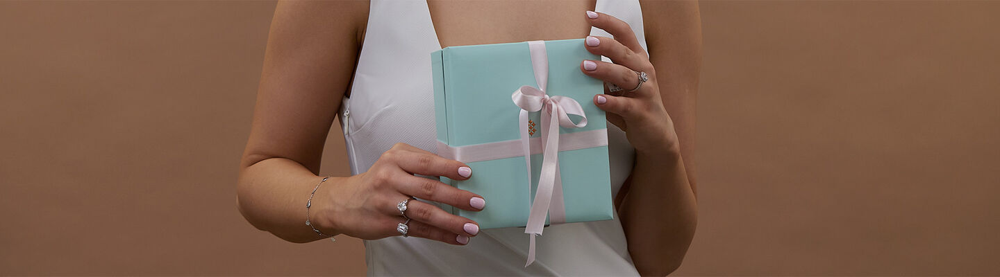 Woman holding a mint green jewellery gift box with pink ribbon, wearing multiple diamond engagement rings and a white dress – Fields proposal gift inspiration